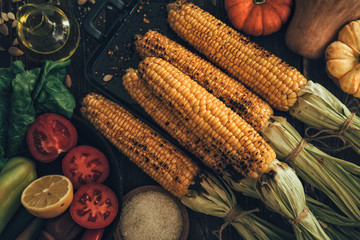 Obraz na płótnie Canvas Summer or autumn food background. Ideas for barbecue and grill parties. Grilled corn, cheese on a dark wooden table. Healthy food, organic, bio, homemade food. Top view.