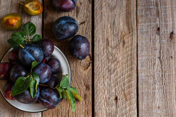 Fresh pile of plums in a old bowl on rustic table with green leaf. Toned image. Soft focus. Copy space.