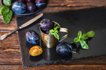 Plums on rustic background. Half and whole of blue plum fruit. Many beautiful plums with leaves. Fresh organic fruits. Food background. Healthy food. Toned image.