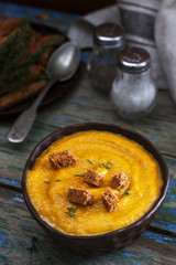 Pumpkin or carrot cream soup with croutons and thyme on a wooden background. Rustic style.