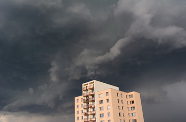 Fototapeta premium Block of flats and stormy sky with dark clouds. Metaphor of negative problem and trouble of real estate. Dangerous weather as threat to house and residential building (Distinctive composition).