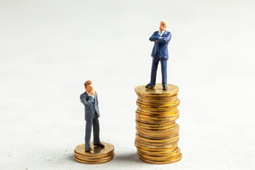 Successful businessman with big profits on stack of gold coins and less successful businessmen with...