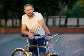 The red bearded man in casual clothes is cycling on the road in the morning city. Healthy lifestyle concept