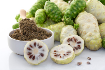 Noni fruit or Morinda Citrifolia with noni slice and noni powder in ceramic bowl and wooden spoon on the white background, it is good source of vitamin edible and delicious for health.