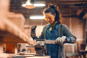Girl working with wood on carpenter bee, wearing protective glasses, smiling.