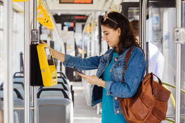 Brunette womanstudent paying with smartphone for the public transport in the tram or bus.