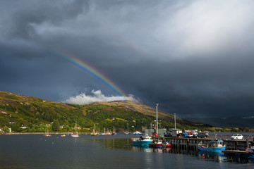 Fototapeta na wymiar Colorful Rainbow Over Fisher Boats In The Picturesque Harbor Of Ullapool In Scotland