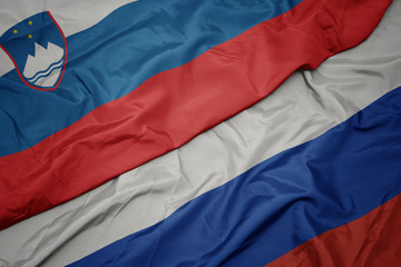 waving colorful flag of russia and national flag of slovenia.