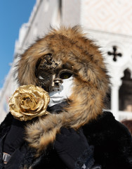 Mysterious hooded mask with a golden rose, posing in Piazza San Marco in Venice during the traditional carnival.