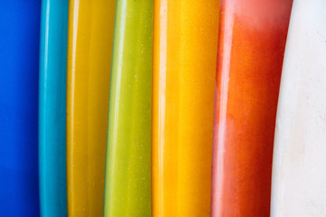 Close up Set of different color surf boards in a stack on sandy beach for rent. Multicolored surfboards as rainbow.