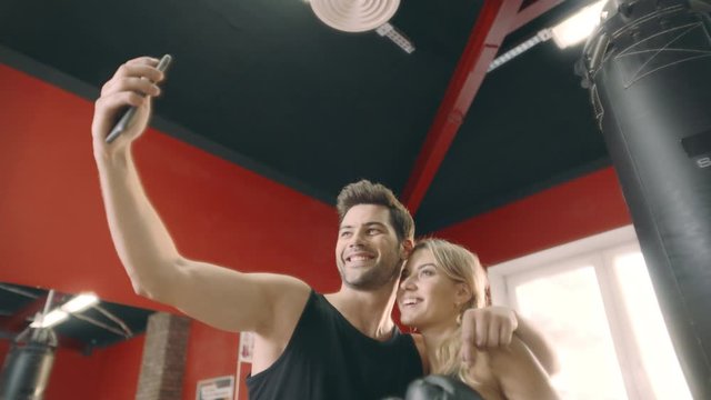 Embracing fitness couple posing to mobile phone for selfie in gym club.