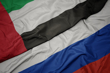 waving colorful flag of russia and national flag of united arab emirates.