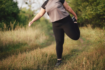 Overweight woman do warming up exercises, stretching legs before running. Runner getting ready for...