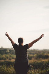 Body positive, freedom, high self esteem, confidence, happiness, inspiration, success, positive affirmation. Overweight woman celebrating rising hands to the sky on summer meadow.