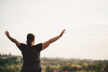 Body positive, freedom, high self esteem, confidence, happiness, inspiration, success, positive affirmation. Overweight woman celebrating rising hands to the sky on summer meadow. - obrazy, fototapety, plakaty