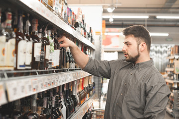 Portrait of a man with a beard wearing a shirt, standing in the alcohol department of the...
