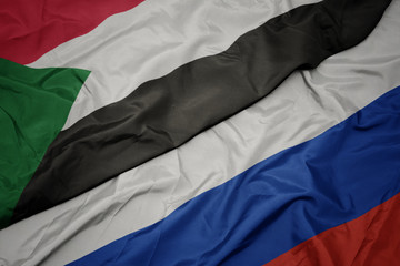 waving colorful flag of russia and national flag of sudan.