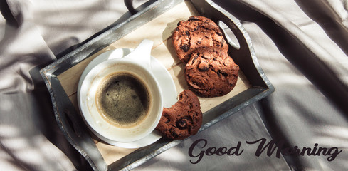 Good morning Female hand holds a cup of coffee on the bed with light linen in a room with natural sunlight and shadow, top view flat lay
