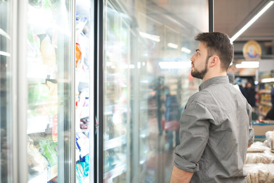 A man chooses frozen foods from shelves in a refrigerator in a supermarket. A man buys products in the store. Shopping in a supermarket concept.