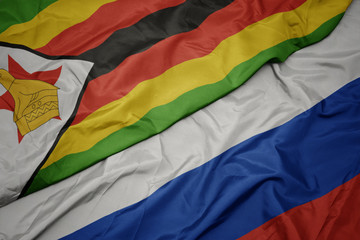 waving colorful flag of russia and national flag of zimbabwe.