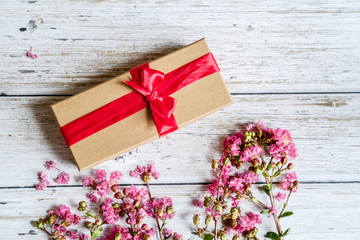 Spring Rustic background with gift box and pink flowers. Copy space on white wood. Valentine day internet sales concept, online shopping holiday background. Mockup, top view, flat lay