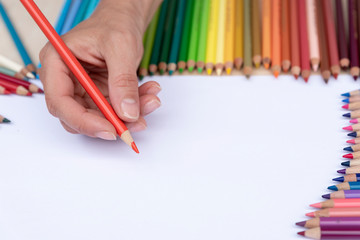 hand with color pencil and row of colorful pencils on a white background with copy space.