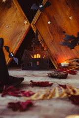 Halloween holiday concept . Lighting paper silhouettes of old castle, ghosts, witch, bats, candles on the wooden background with autumn dry leaves. Vertical spooky holiday card. Copy space.