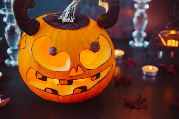 Close up carved luminous pumpkin with scary evil face, burning candles and paper silhouettes of...