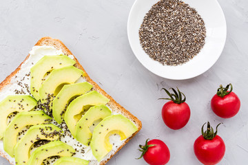 Snacks with avocado. Avocado toast with chia seeds and cream cheese, cherry tomatoes on table. Healthy breakfast lying on gray concrete background. Mockup, flat lay, top view with copy space