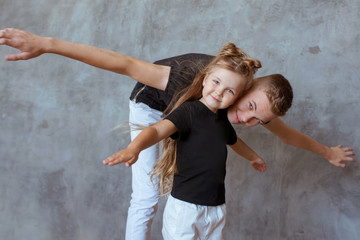 Obraz na płótnie Canvas caucasian siblings - teenager boy brother and little girl sister playing in aircraft in modern loft interior on gray cement background