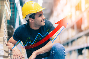Smart Indian engineer man wearing safety helmet doing stock tick check and cardboard stock product management in factory warehouse background and profit chart grow up