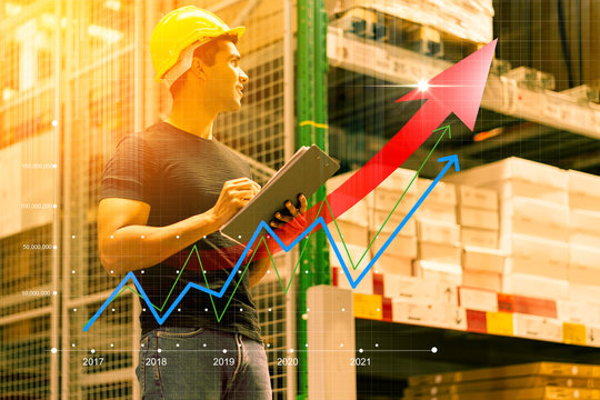Smart Indian engineer man wearing safety helmet doing stock tick check and cardboard stock product management in factory warehouse background and profit chart grow up