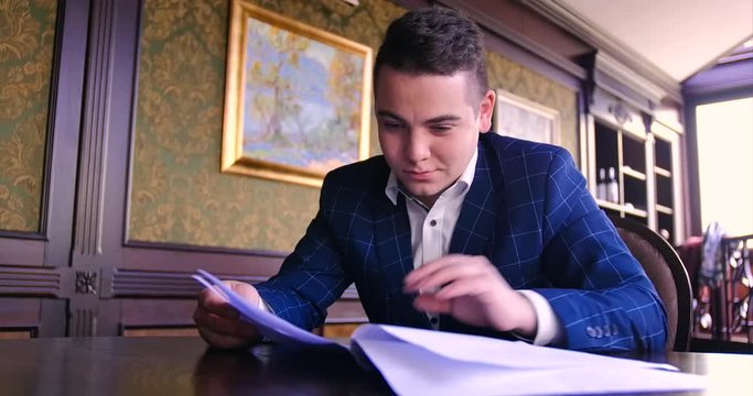 A young businessman sits in a chic office and is dissatisfied with a paper contract, refuses to sign, angry, unfavorable conditions, a torn deal. Wooden table, elite, emotions, discontent