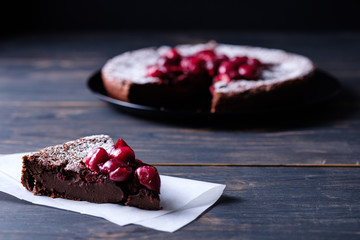 A slice of chocolate clafouti with a cherry on a wooden table. French delicious dessert.