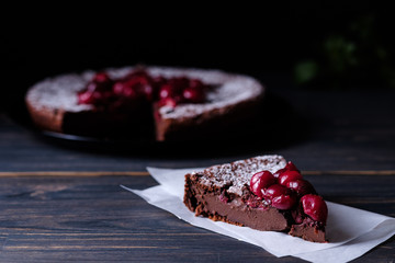 A slice of chocolate clafouti with a cherry on a wooden table. French delicious dessert.