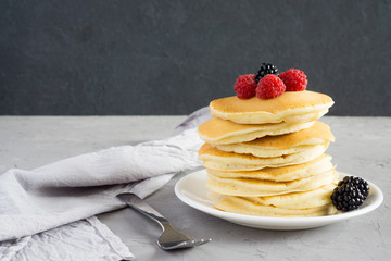 American pancakes with raspberries and blackberries for breakfast on a gray concrete background with copy space