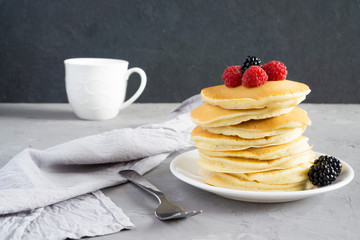 American pancakes with raspberries and blackberries for breakfast on a gray concrete background with copy space