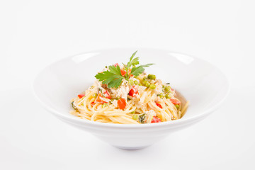 Spaghetti with cream sauce with smoked mackerel, peas ,bell pepper and some parsley on a white plate on a white background