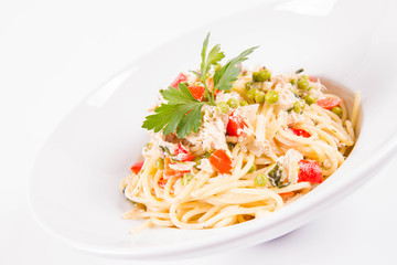 Spaghetti with cream sauce with smoked mackerel, peas ,bell pepper and some parsley on a white plate on a white background