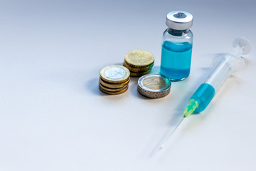 SARS-COV-2: Spritze und Ampulle mit neu entwickeltem Medikament und EURO-Geldmünzen zeigen...