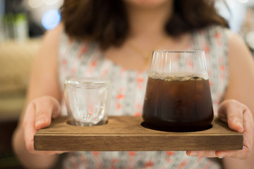 hand of woman holding a cup of americano coffee and cold water on Wooden tray, cold brew coffee and black coffee