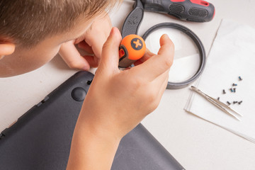 A boy of 10 years old is sorting a laptop for cleaning and maintenance. Selective focus. Screwdrivers, purge cylinder, magnifying glass and spray cleaner in the frame.