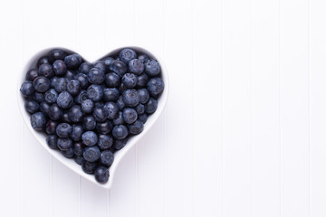 Fresh blueberries, in a heart shaped bowl on a wooden background.