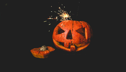 orange pumpkin on black background . cut out the eyes and mouth . the shining light is on.