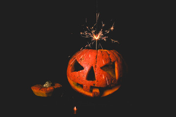 orange pumpkin on black background . cut out the eyes and mouth . the shining light is on.