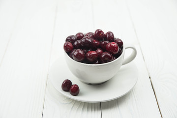 A lot of fresh sweet cherry fruit berries with water drops, close up in tea cup on white background. Close up of pile of ripe cherries. Large collection of fresh red cherries. Ripe cherries texture