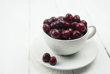 A lot of fresh sweet cherry fruit berries with water drops, close up in tea cup on white background. Close up of pile of ripe cherries. Large collection of fresh red cherries. Ripe cherries texture
