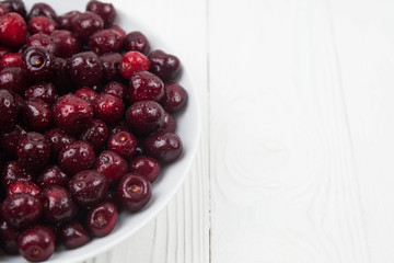 A lot of fresh sweet cherry fruit berries with water drops, close up on the plate on white background. Close up of pile of ripe cherries. Large collection of fresh red cherries. Ripe cherries texture 
