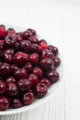 A lot of fresh sweet cherry fruit berries with water drops, close up on the plate on white background. Close up of pile of ripe cherries. Large collection of fresh red cherries. Ripe cherries texture 