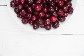A lot of fresh sweet cherry fruit berries with water drops, close up on the plate on white background. Close up of pile of ripe cherries. Large collection of fresh red cherries. Ripe cherries texture 